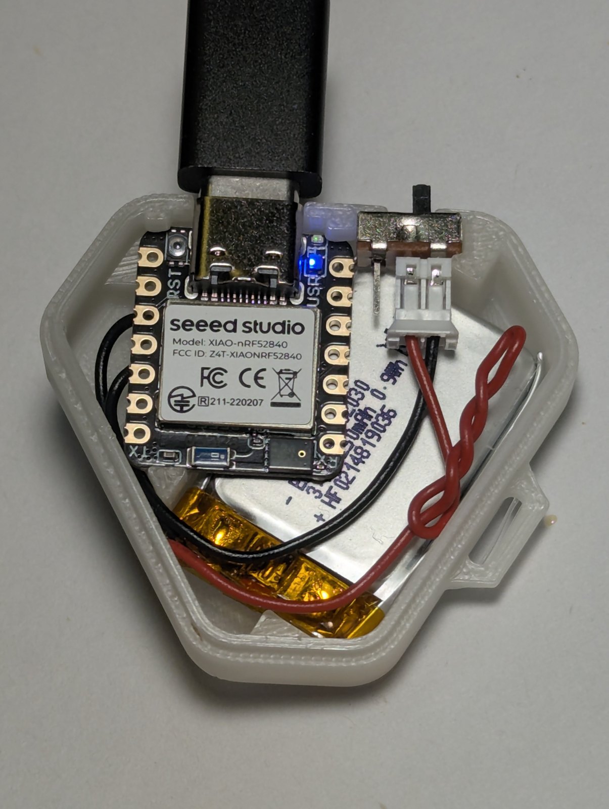 Opened Mobido wearable showing the Seeed XIAO board, battery, and switch